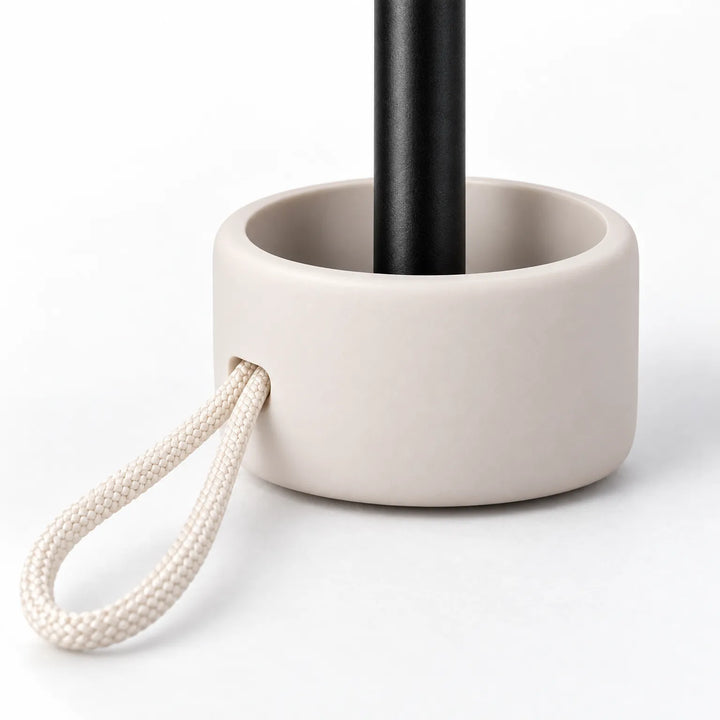 Close-up of the umbrella handle: a rounded cream base around a black shaft, with a braided cream cord loop threaded through. 5