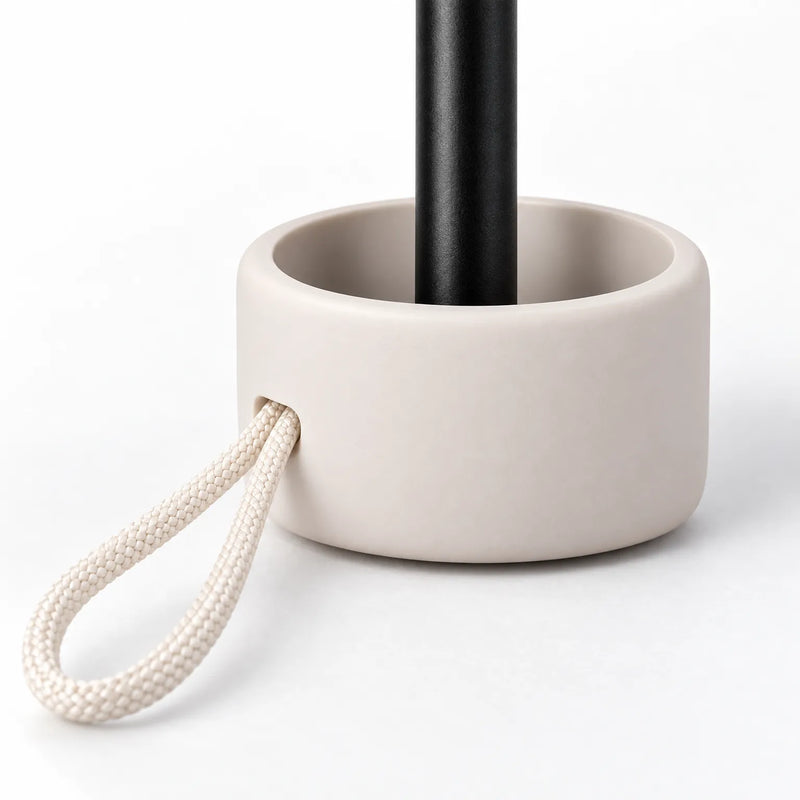 Close-up of the umbrella handle: a rounded cream base around a black shaft, with a braided cream cord loop threaded through. 5
