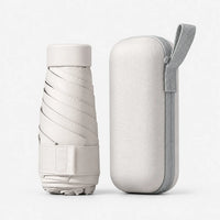 Cream folded umbrella with its cap and strap beside a matching hard zippered case with a grey wrist loop, on white. 6