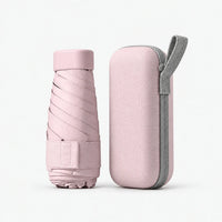 Pale pink folded umbrella with cap and strap standing next to a matching hard zippered case with a grey loop, on white. 9