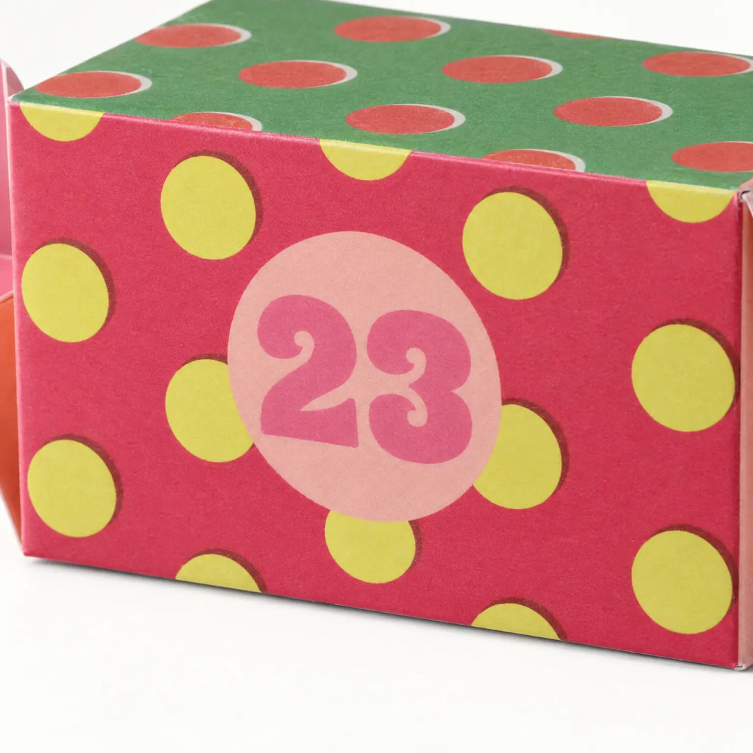 Close-up of one pink paper box with yellow polka dots, a round numbered sticker and a green dotted top. 3