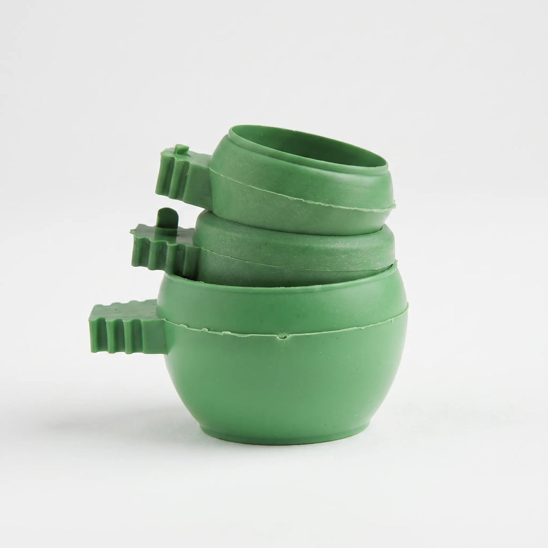 Three green plastic bowls stacked together, each with a ridged clip handle on the side, against a plain white background. 1