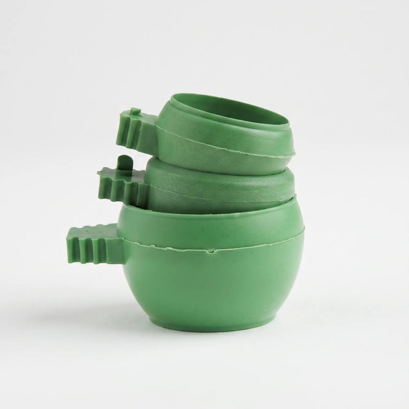 Three green plastic bowls stacked together, each with a ridged clip handle on the side, against a plain white background. 1