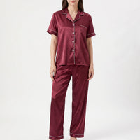 Front view of a model in the burgundy satin pyjama set, showing the button-up top, chest pocket and white piping. 2