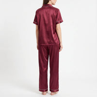 Back view of the burgundy satin pyjama set on a model, showing the plain back of the shirt and long trousers. 3