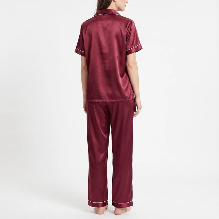 Back view of the burgundy satin pyjama set on a model, showing the plain back of the shirt and long trousers. 3