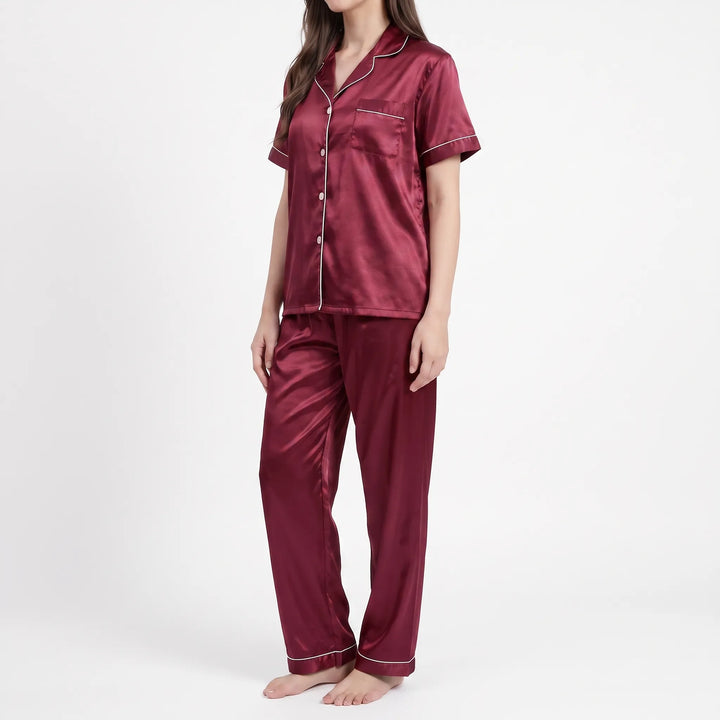 Three-quarter side view of a model in the burgundy satin pyjamas, showing the notched collar, pocket and straight-leg trousers. 4