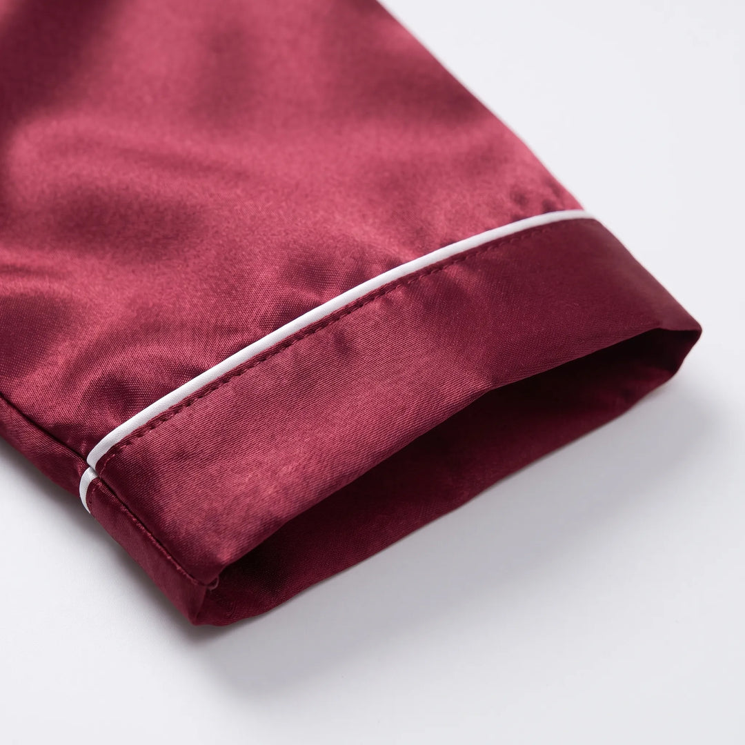 Close-up of a burgundy satin sleeve cuff with white piping and neat stitching, laid flat on a white surface. 5
