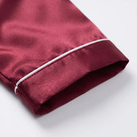 Close-up of a burgundy satin sleeve cuff with white piping and neat stitching, laid flat on a white surface. 5