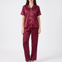 Studio front view of a model wearing the burgundy satin pyjama set with contrast white piping and white buttons. 6