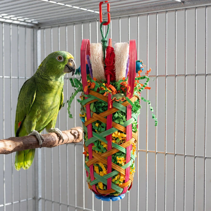 Toy hanging in a wire cage next to a green parrot perched on a wooden branch, showing its size. 3