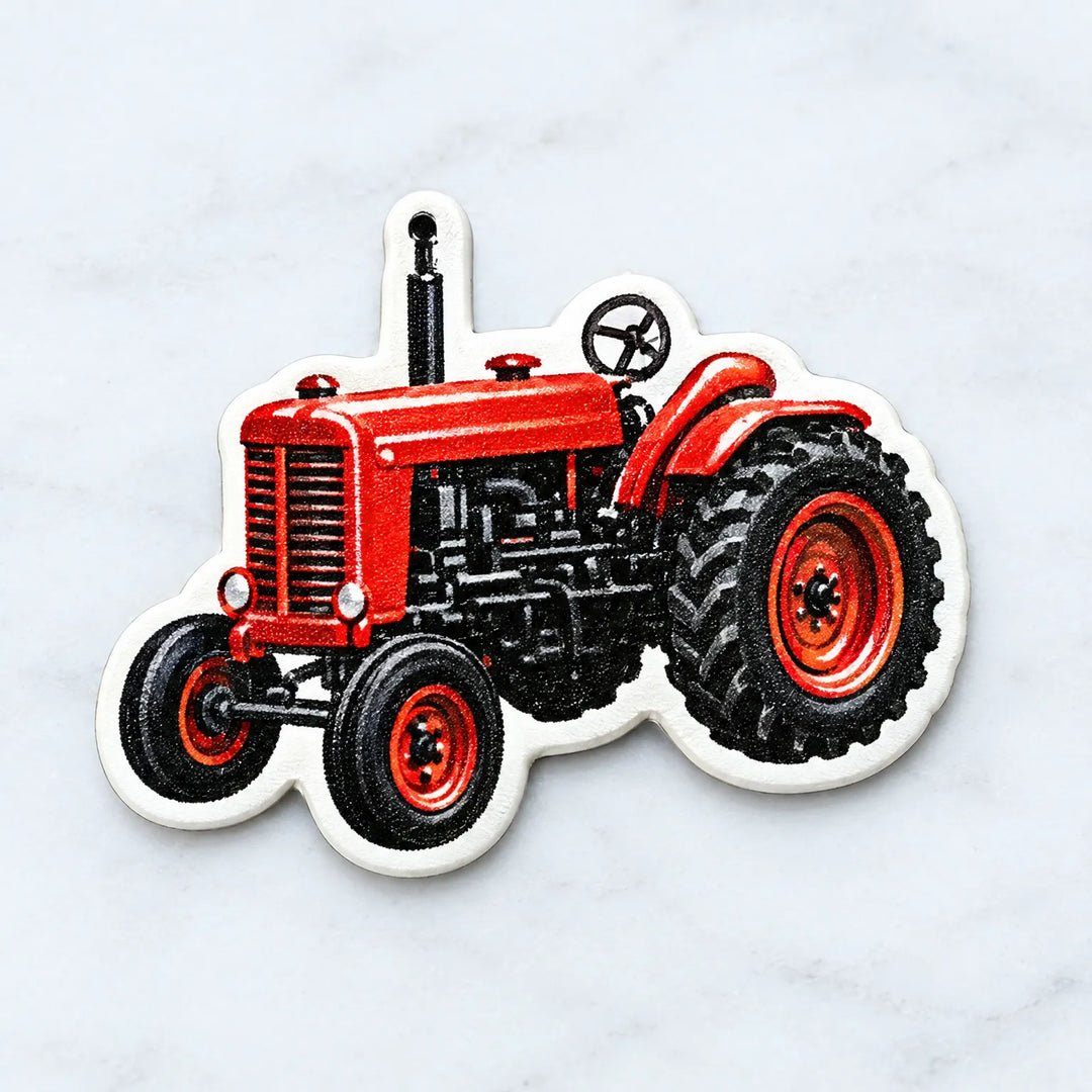 Close-up of a single red vintage tractor ornament with a white border and a small hanging hole at the top, on a marble surface. 3