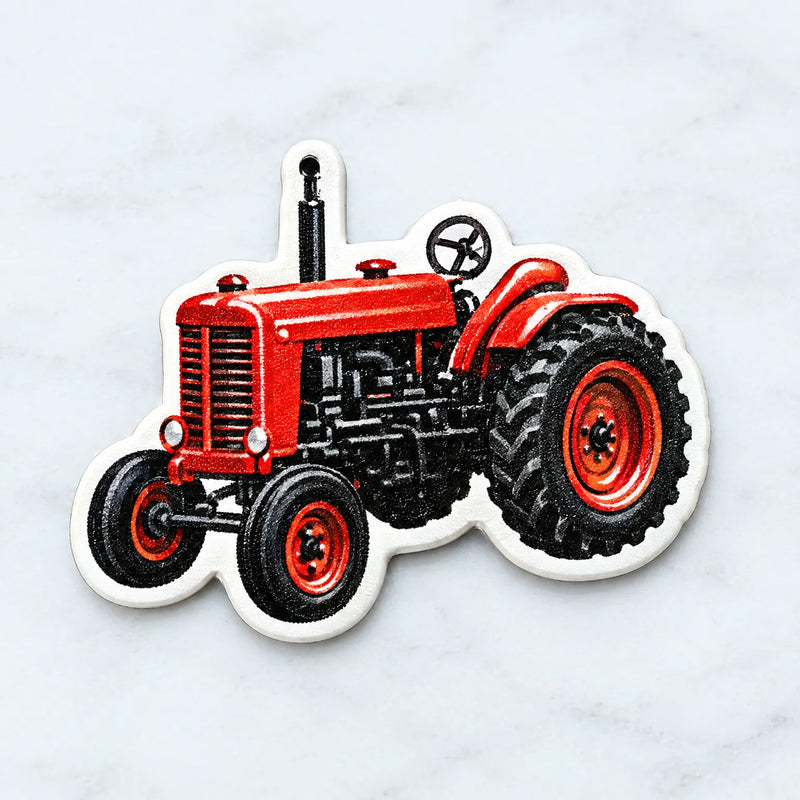 Close-up of a single red vintage tractor ornament with a white border and a small hanging hole at the top, on a marble surface. 3
