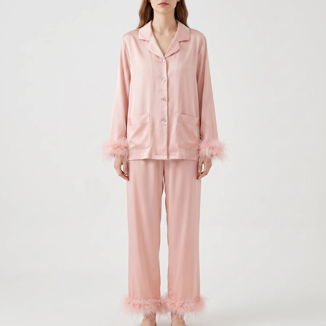 Front view of a woman wearing the pink satin pyjama set, showing button front, two patch pockets and feather-trimmed cuffs and hems. 2