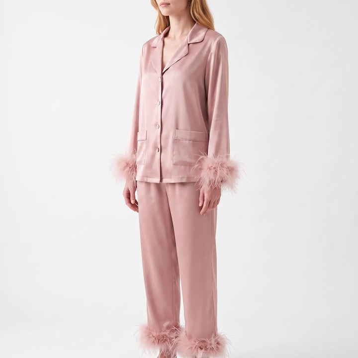 Model wearing the pyjama set in a deeper dusty pink satin, seen from the side with feather-trimmed cuffs and trouser hems. 6