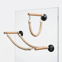 Two wooden perches with black suction cups and twisted cotton ropes stuck to a glass pane, one short and one long. 1