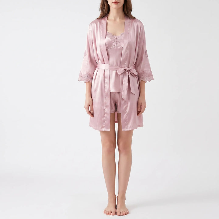 Model standing in a pink satin robe with lace-trimmed sleeves worn open over a matching camisole and shorts. 2