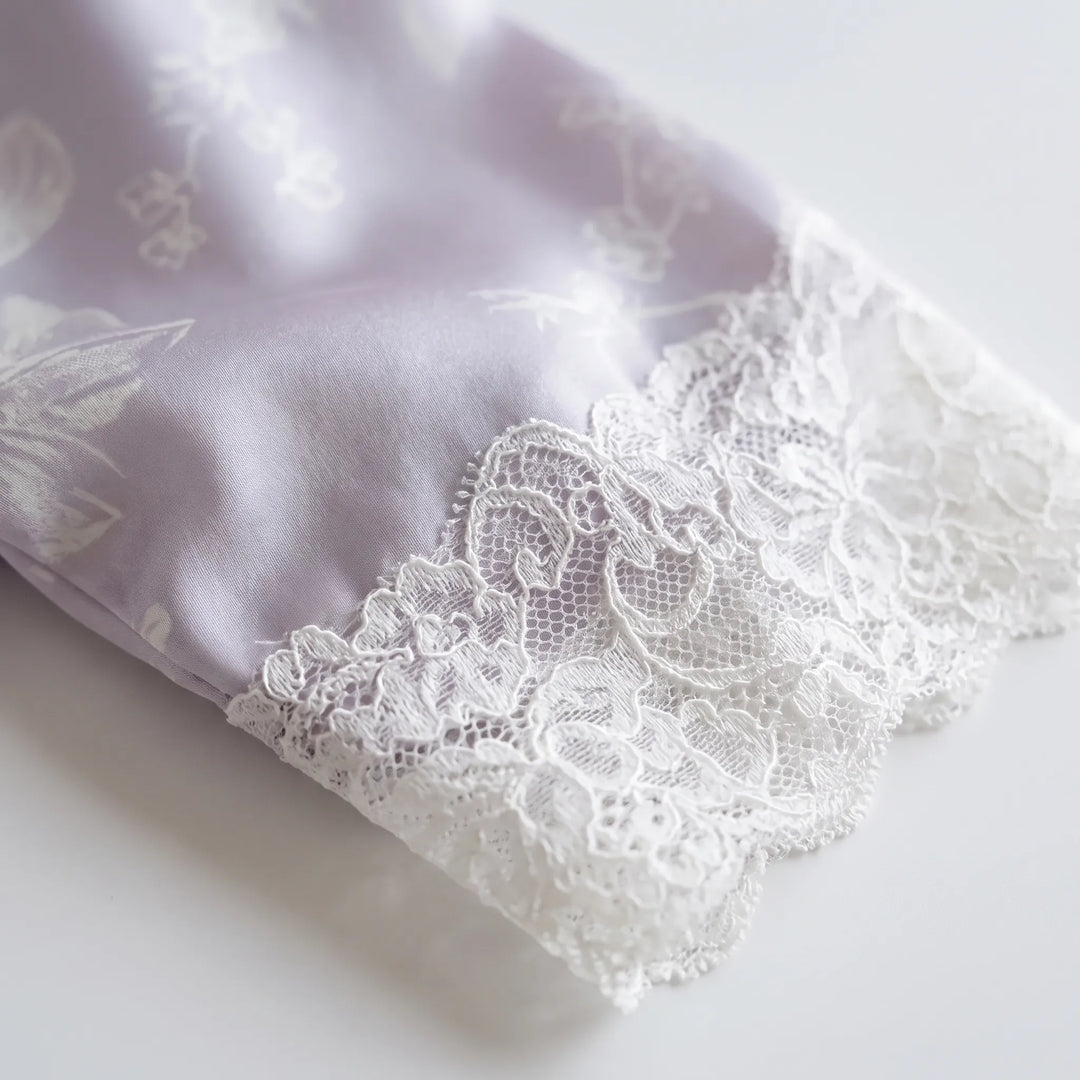 Close-up of a sleeve cuff with white scalloped lace trim against the smooth lilac fabric with faint floral print. 5
