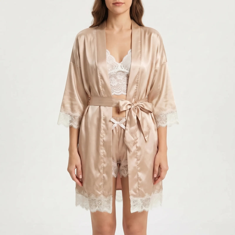 Front view of a model on a plain light background wearing the belted satin robe over lace top and shorts. 2