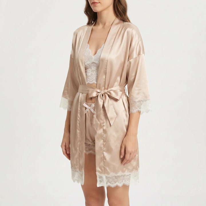 Three-quarter side view of a model wearing the satin robe tied with a bow over the lace bralette and shorts. 4