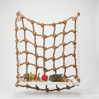 Natural rope climbing net hung by white plastic chains above a white platform holding colourful toys, shown against a plain background. 1