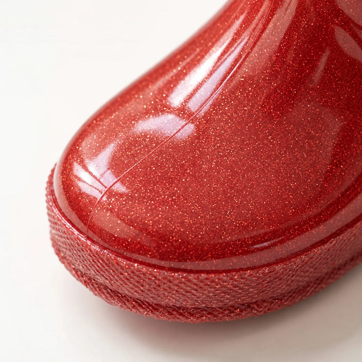 Close-up of the toe of a red glitter rain boot showing the sparkling glossy surface and textured sole edge. 6