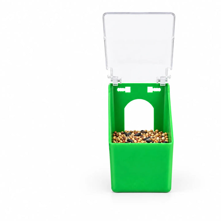 Front view of the green plastic feeder with its clear lid flipped open, showing seed mix inside and an arched opening. 1