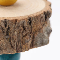 Close-up of one wooden slice showing its rough bark edge and pale growth rings, with a yellow bead above and a teal bead below. 3