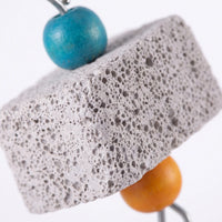 Close-up of the pitted, porous texture of a grey stone block between a blue wooden bead and an orange one. 4