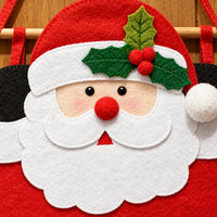 Close-up of Santa's face on the felt calendar, with white beard, red pom-pom nose, holly leaves with berries and stitched edges. 3