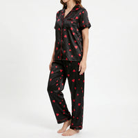 Three-quarter side view of a model in the black satin pyjamas, showing the red piping, chest pocket and buttoned front. 4