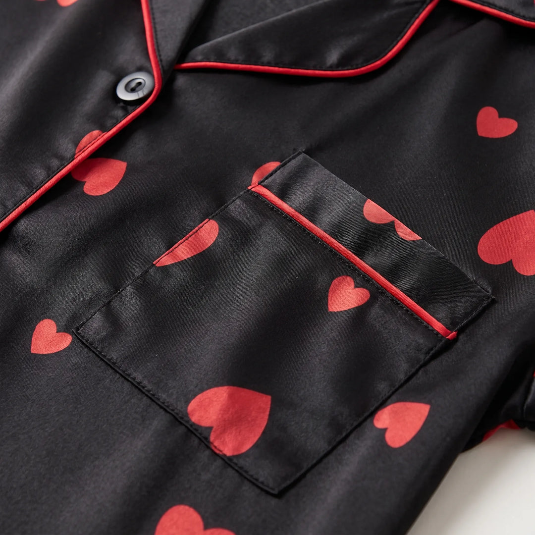 Close-up of the shirt's chest pocket, red piped collar edge, black button and scattered red heart print on glossy black satin. 5