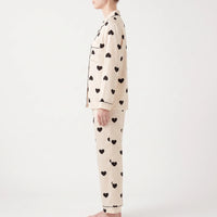 Side view of a model wearing the long-sleeve heart print pyjama top and trousers, showing the chest pocket and cuff piping. 3