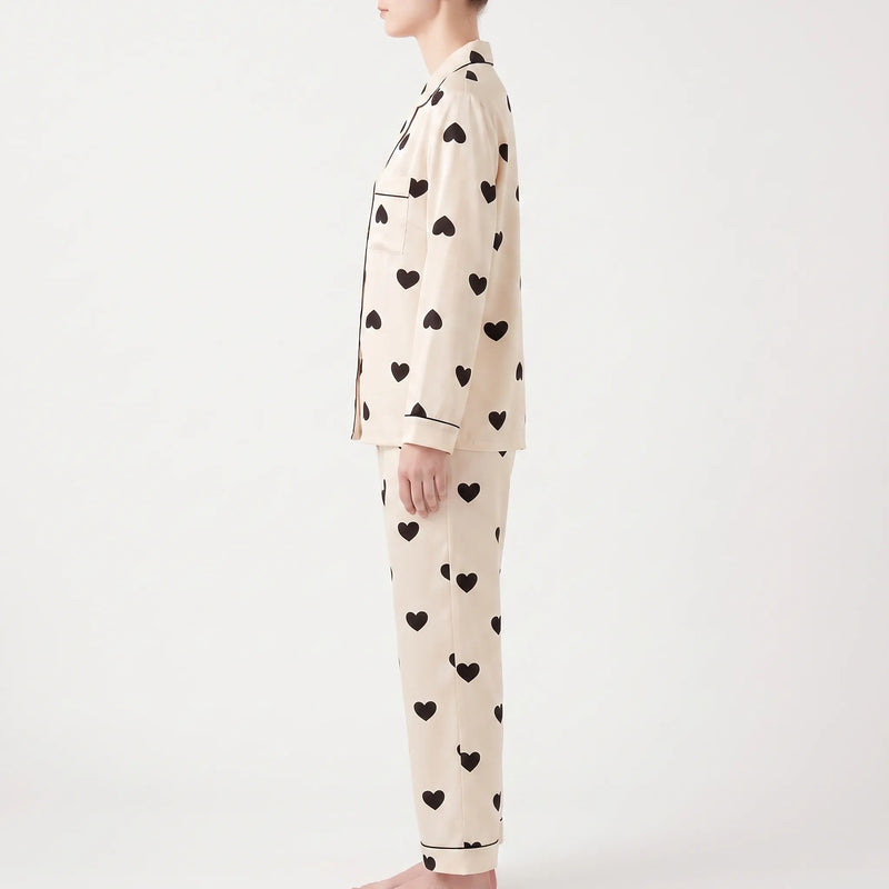 Side view of a model wearing the long-sleeve heart print pyjama top and trousers, showing the chest pocket and cuff piping. 3