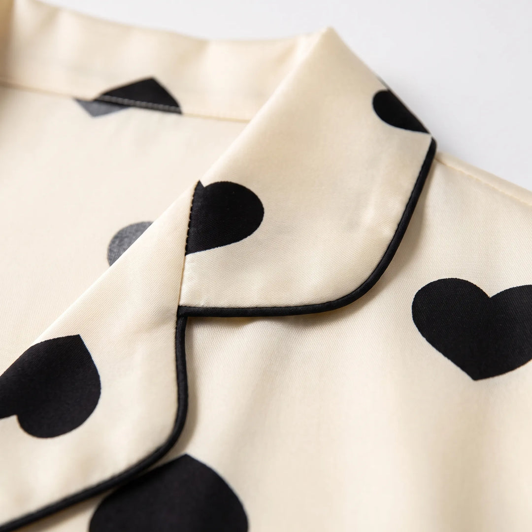 Close-up of the notched collar with black piping and scattered black hearts on cream satin-look fabric. 4