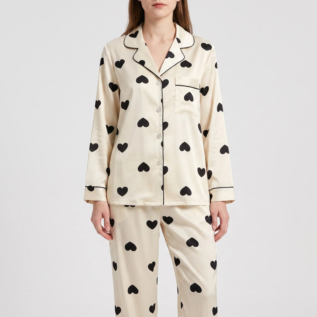 Front view of a model in the long-sleeve heart print pyjama shirt and trousers, buttoned, with chest pocket and black piping. 6
