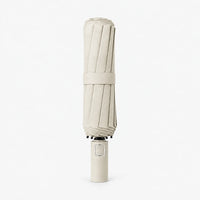 Folded cream-colored umbrella with a matching strap and handle, shown upright on a white background. 10