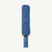 Folded denim blue umbrella standing upright on a white background, canopy secured by a fabric strap. 11