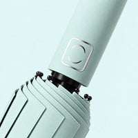 Close-up of a mint green umbrella handle with its square metallic emblem, canopy stitching and black rib tips. 5