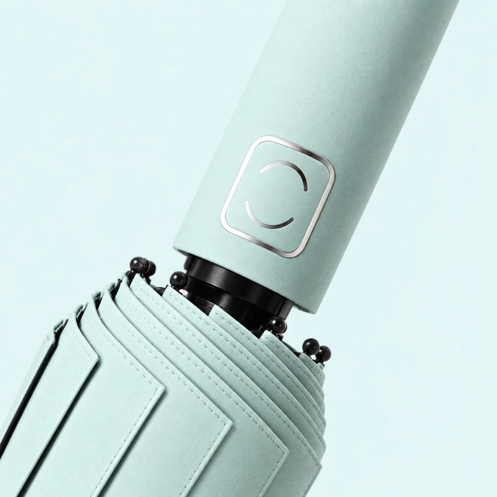 Close-up of a mint green umbrella handle with its square metallic emblem, canopy stitching and black rib tips. 5