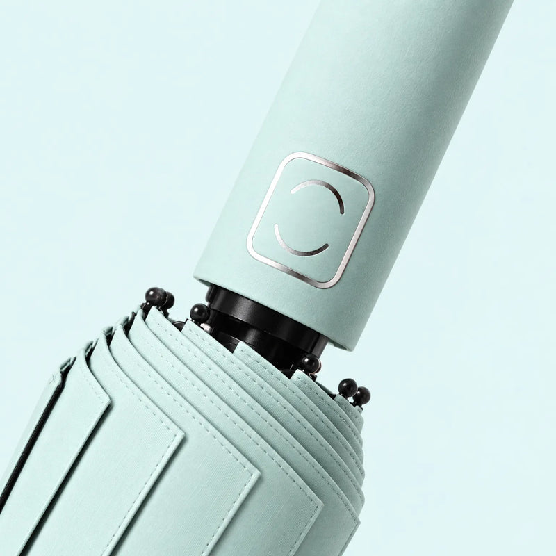 Close-up of a mint green umbrella handle with its square metallic emblem, canopy stitching and black rib tips. 5