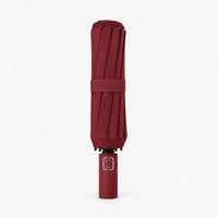 Folded dark burgundy umbrella standing upright on a white background, closed with a matching strap. 9
