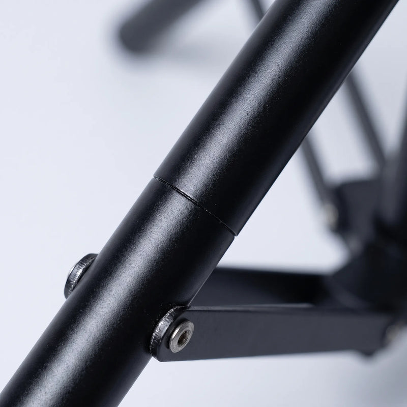 Close-up of a matt black tubular tripod leg with a metal joint, screws and a brace arm, softly blurred background. 3