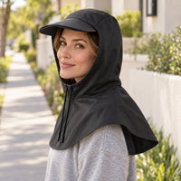 Woman in a black hooded rain cape with a peaked brim and drawstring, glancing over her shoulder on a sunny sidewalk. 1