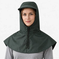 Front view of a dark green hooded cape with a front zip, drawstring toggles and a short brim, worn over a grey top. 2