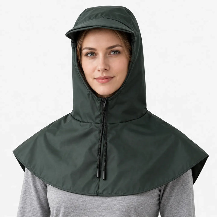 Front view of a dark green hooded cape with a front zip, drawstring toggles and a short brim, worn over a grey top. 2