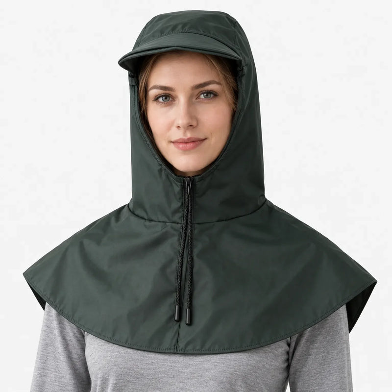 Front view of a dark green hooded cape with a front zip, drawstring toggles and a short brim, worn over a grey top. 2