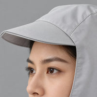 Close-up of a light grey hood's stitched peaked brim and side panel, framing a woman's eye and brow against a grey background. 5