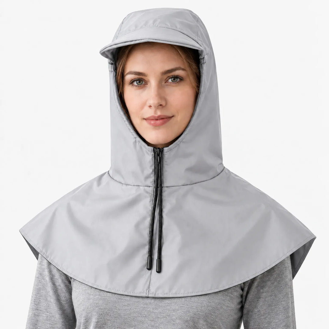 Front view of a light grey hooded cape with a zip, black drawstring cords and a brim, worn over a grey top. 6