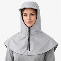 Front view of a light grey hooded cape with a zip, black drawstring cords and a brim, worn over a grey top. 6